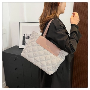 Side view of a quilted nylon tote bag with leather trim and Fashion lettering detail