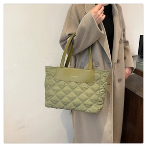 Detail of green quilted nylon tote bag with golden fashion letter patch and long handles