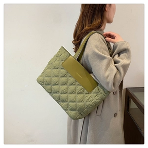 Close-up of olive green quilted tote bag with FASHION lettering on a stylish coat