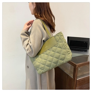Detailed view of green quilted down tote bag with a fashion patch in a work office setting