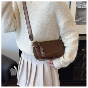 Detail of dark brown pebble leather crossbody bag with vintage jacquard strap over a sweater