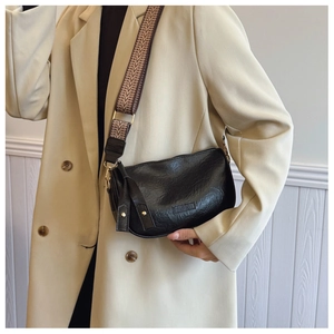 Close-up of black textured leather crossbody bag with patterned wide shoulder strap