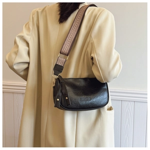 Detail of black matte pleated leather bag with a geometric pattern wide strap worn by a model