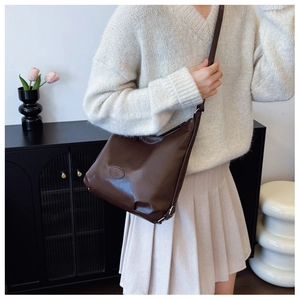 Detail of dark brown leather tote bag with embossed logo worn as an underarm shoulder bag