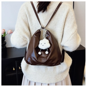Brown faux leather tote bag with white cloud plush charm shown in a cozy home setting
