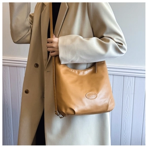 Detail of caramel hobo bag with adjustable strap and oval fashion emblem on the side