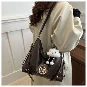 Detail of dark brown tote bag with metallic M emblem and plush white cloud charm