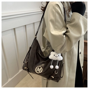 Detail of dark brown leather tote with gold M logo and white plush cloud charm accessory