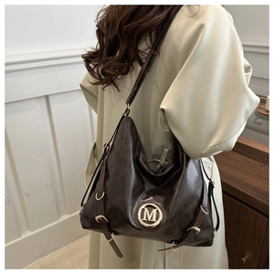 Detail of a deep brown leather Hobo bag featuring a gold M-logo and decorative side straps