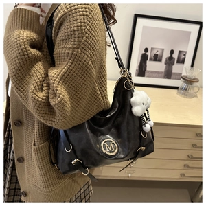 Detail of black leather crescent bag featuring a gold M logo and cloud plush charm