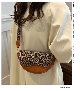 Detail of leopard print wide strap and brown leather saddle bag with golden hardware