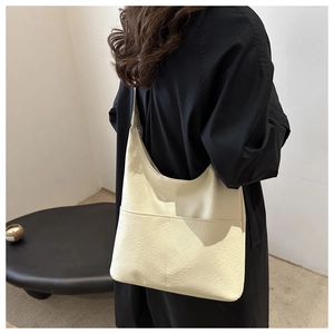 Detail of a beige oversized hobo tote bag in pleated PU leather worn by a model