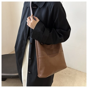 Detail view of large brown faux leather tote bag with front pocket shown on a model