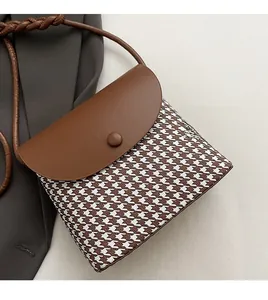Close-up of houndstooth crossbody bag with brown leather flap and woven shoulder strap