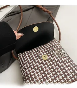 Close-up of golden magnetic buckle on brown houndstooth crossbody bag with fine details