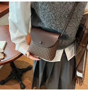 Detail of vintage houndstooth crossbody bag with brown leather flap on a wooden table