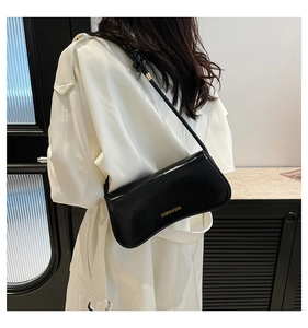 Detalle del bolso de hombro en charol negro brillante con eslogan dorado impreso