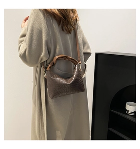 Detail of dark brown woven handbag with knotted handle and elegant gold hardware