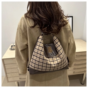 Detail of vintage plaid backpack featuring cute teddy bear embroidery and brown leather trim