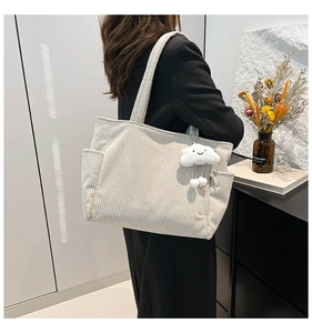 Detail of beige corduroy tote bag with side pocket and cloud plush charm on model