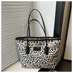 Close-up of leopard print canvas tote bag with black shoulder straps and leather patch