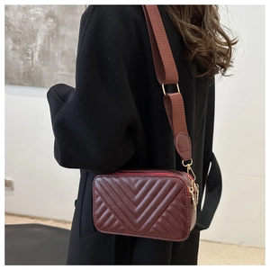 Detail of burgundy quilted square bag with adjustable brown wide shoulder strap and gold hardware