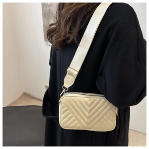 Detail of ivory quilted crossbody bag with V-shaped stitching and wide woven strap