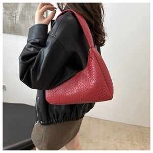Close-up of red crescent underarm bag in crocodile pattern leather on model's shoulder