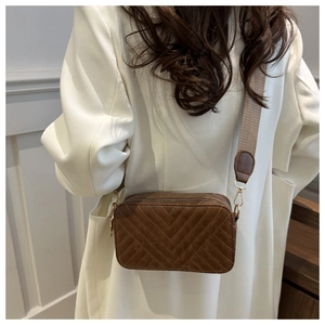 Close-up of brown V-quilted crossbody bag with dual zippers and wide fabric strap