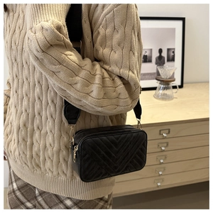 Close-up of black quilted crossbody bag with gold hardware worn over a beige sweater