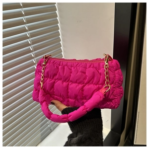 Detail of rose red quilted puffer bag with golden chain and soft fabric handle texture