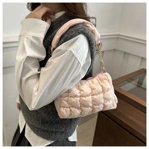Detail of light pink quilted bubble bag featuring padded handles and gold chain accents