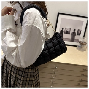 Detail of a black quilted puffer bag with metal chain strap worn on shoulder