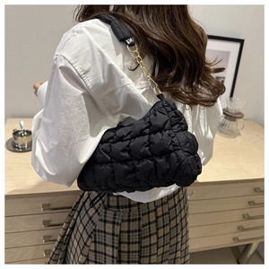 Close-up of black quilted puff shoulder bag with gold chain strap on a female model