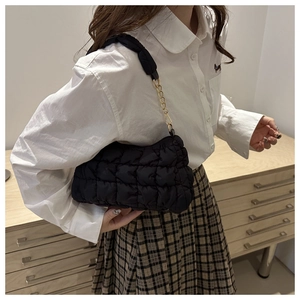 Detailed view of black quilted cloud bag with gold chain strap worn by a female model