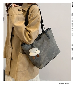 Detail of grey suede tote bag with black handles and a white cloud plush charm