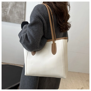 Detailed side view of large beige tote bag with brown straps worn with grey coat