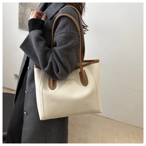 Detail of a large cream and brown PU leather tote bag with contrast stitching on a model