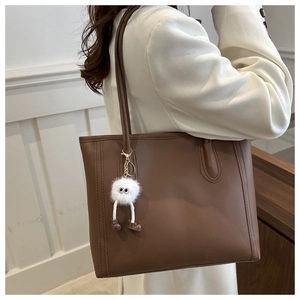 Deep brown faux leather tote bag detail with fine stitching and a cute plush monster charm