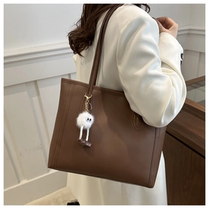 Brown leather tote bag featuring a cute white plush monster pendant and slim shoulder straps