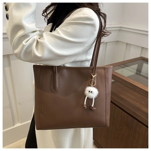 Detail of brown PU leather tote bag with a white plush monster charm on a white coat