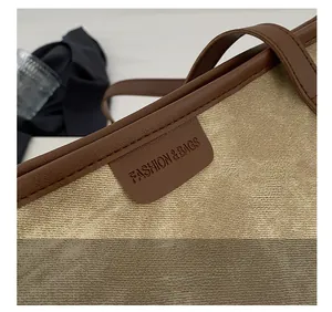 Close-up of beige canvas tote bag detailing brown leather trim and embossed text