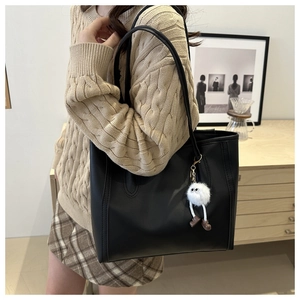 Detail of a large black tote bag with white monster charm on a cozy beige sweater