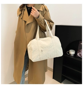 Close-up of white nylon tote bag with front zipper pocket shown on a trench coat model