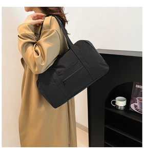 Close-up of black nylon tote bag showing side view and zipper pocket on model