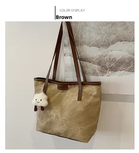 Detail of brown canvas tote bag featuring leather handles and a white cloud charm