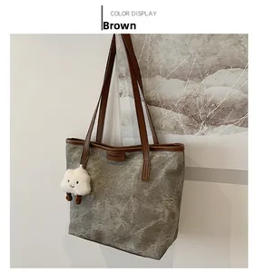Detail of grey tote bag with brown leather handles and plush cloud pendant accessory