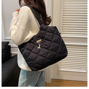 Detail of black quilted tote bag with golden deer pendant and metal hardware detail