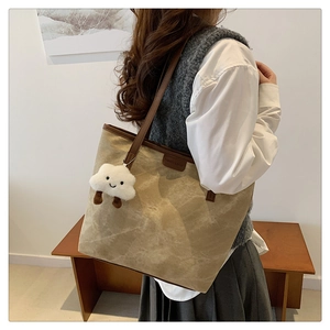 Detail of khaki tote bag with brown leather patch and white plush cloud pendant