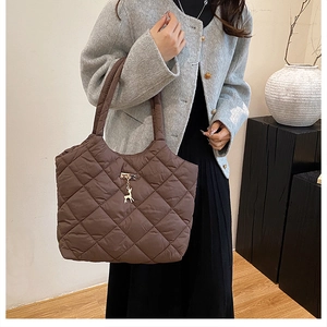 Detail of a brown quilted puffer tote bag featuring a metal deer charm and diamond stitching